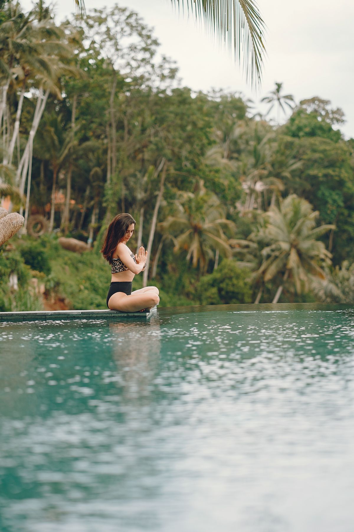A woman meditating at the edge of a tropical infinity pool
